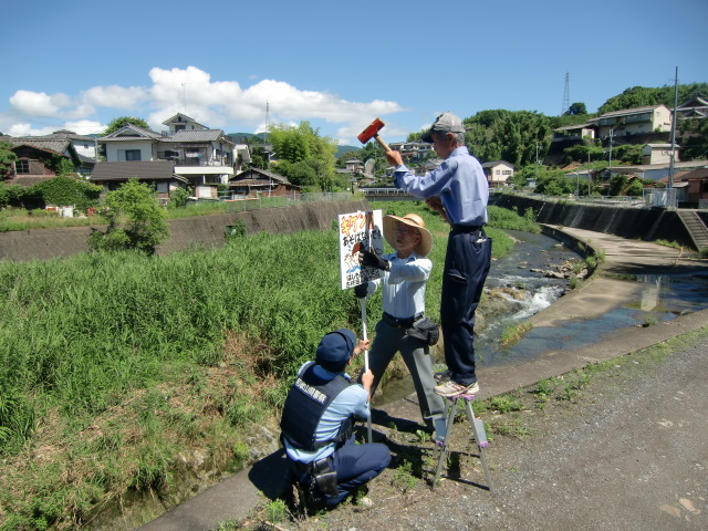 橋本川に水の事故注意の看板を立てる地元住民とお巡りさん