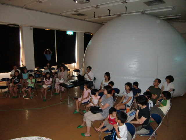 モバイルプラネタリウムのそばで山本会長の「宇宙」の話を聴く親子たち