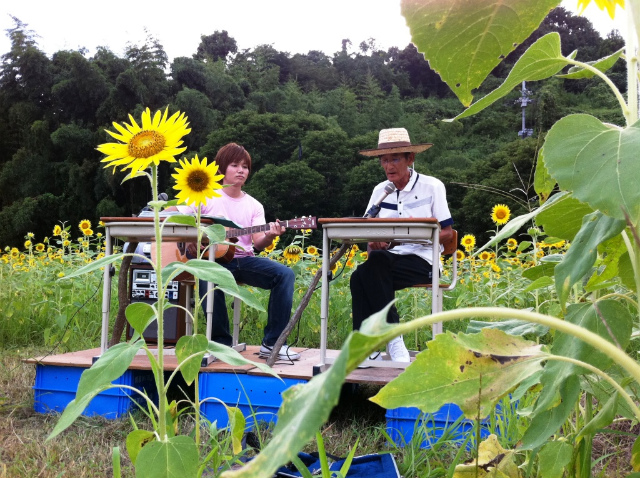 ひまわり畑でギターを演奏する白石さん(左)と大野さん