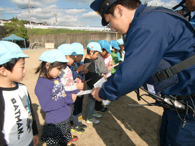 園児たちに塗り絵はがきを配布する橋本駅前交番のお巡りさん